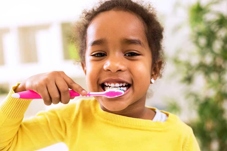 Young black girl in a yellow top brushing her teeth with a pink toothbrush